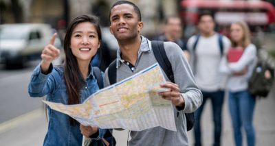 Happy multi-ethnic couple sightseeing in London and holding a map looking for directions. Map was designed from scratch by us.
